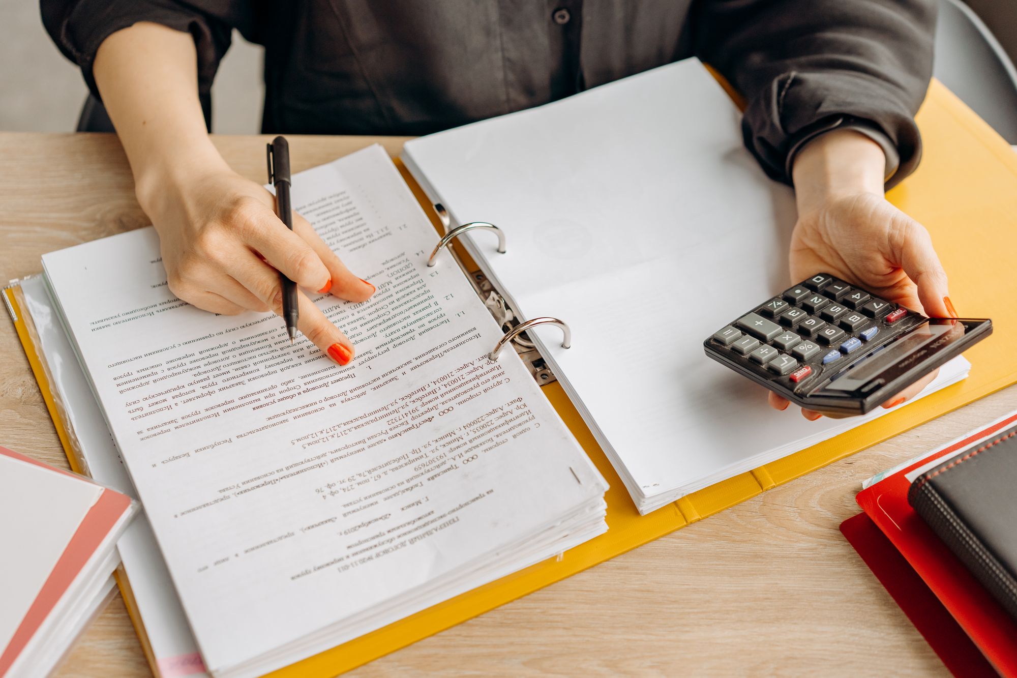 An accountant working through a binder of figures with a pen and calculator